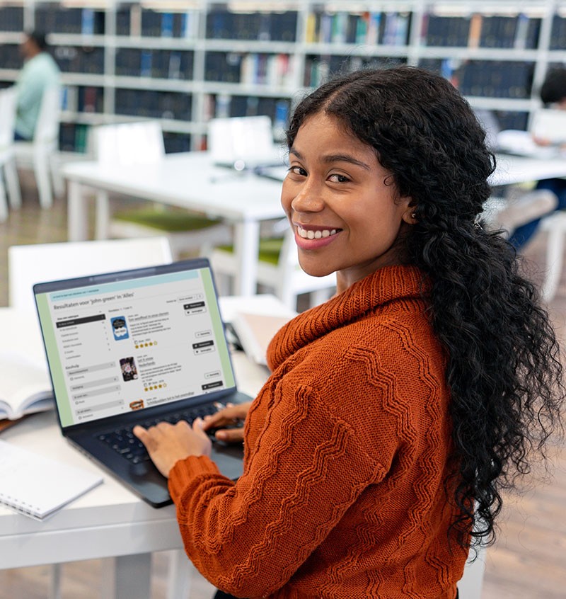 Lachende vrouw met laptop waarop de mediatheekWise-portal te zien is, in een bibliotheek