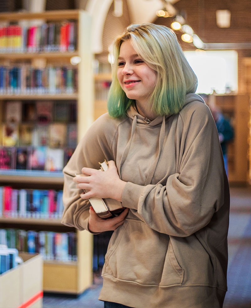 Glimlachende vrouw met boek in een bibliotheek